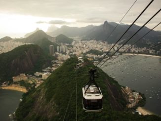 An aerial view of Rio de Janeiro's skyline with a cable car descending from Sugarloaf Mountain at sunset.