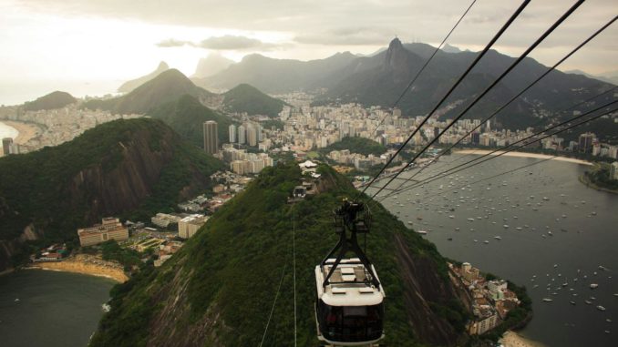 Photo by Aline Cardoso An aerial view of Rio de Janeiro's skyline with a cable car descending from Sugarloaf Mountain at sunset.